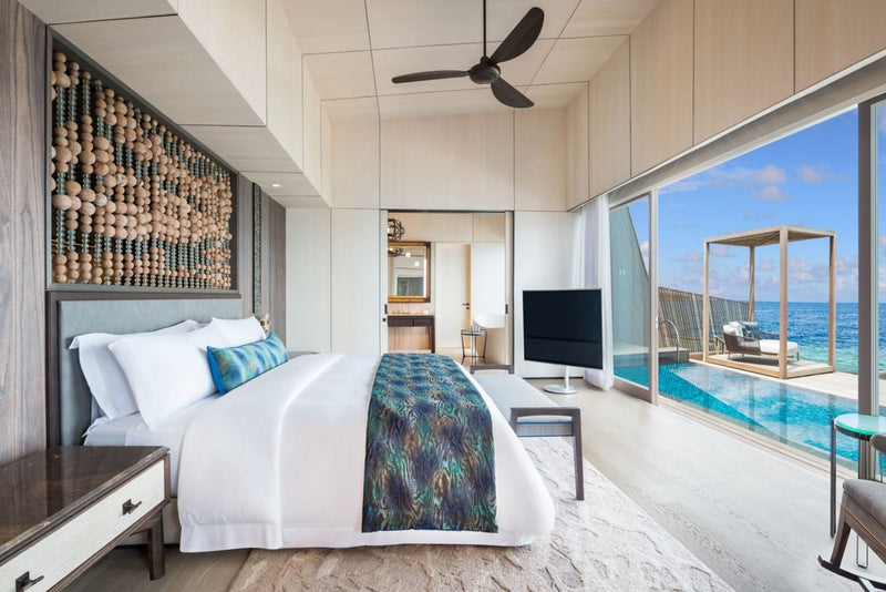 A bedroom at The St. Regis Maldives Vommuli with glass onto a private deck, a pool and a shaded daybed.