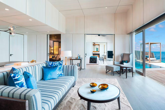 The St. Regis Maldives Vommuli, Dhaalu Atoll — Living room with a striped sofa and glass doors onto the deck and pool