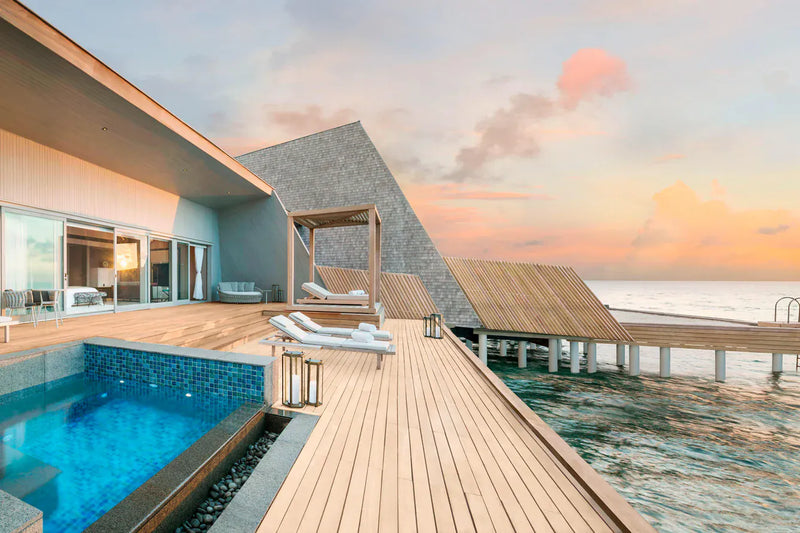An overwater villa deck at The St. Regis Maldives Vommuli at dusk, its pool and timber walkway with other villas beyond.