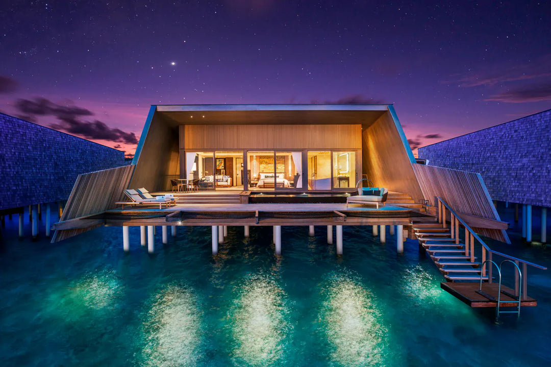 The St. Regis Maldives Vommuli, Dhaalu Atoll — Overwater villa lit at night, its pool glowing under a star-filled sky