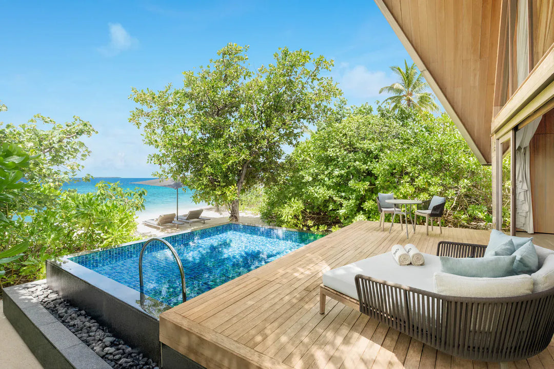 The St. Regis Maldives Vommuli, Dhaalu Atoll — Deck with an infinity pool and a daybed, looking through palms to the beach