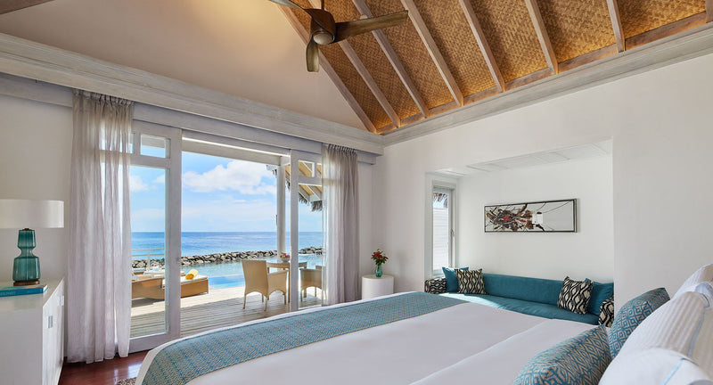 NH Maldives Kuda Rah Resort, South Ari Atoll: the bedroom of a One Bedroom Over Water Pool Villa, with glass doors onto the deck and the sea.