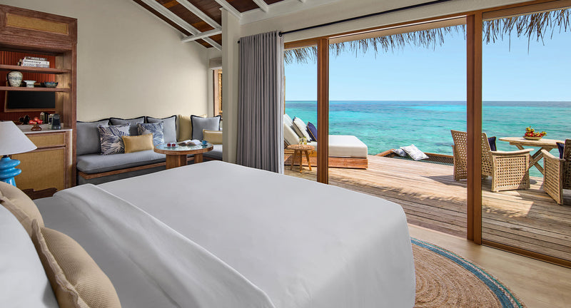 NH Collection Maldives Reethi Resort, Baa Atoll: the bedroom of an Over Water Villa, with sliding doors onto the deck and the sea.