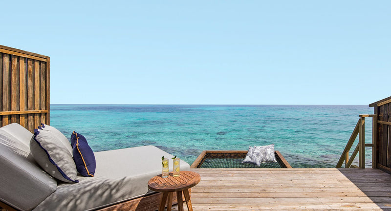 NH Collection Maldives Reethi Resort, Baa Atoll: the deck of an Over Water Villa, with a sun lounger and steps down to the lagoon.