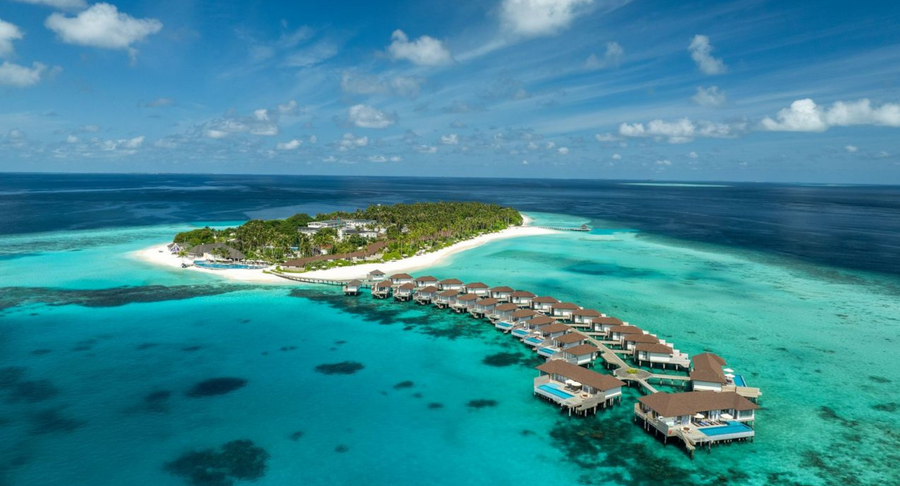 A long curving jetty of overwater villas at Avani+ Fares Maldives, seen from the air with the island behind.