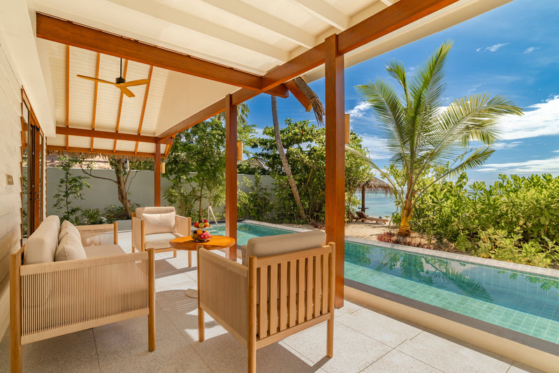 The shaded veranda of an Earth Pool Residence at OZEN LIFE Maadhoo, timber armchairs beside the pool with the beach beyond