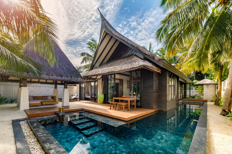 A two-bedroom Earth Pool Pavilion at OZEN RESERVE BOLIFUSHI, a thatched timber villa with a tiled pool, dining deck and shaded daybed among the palms