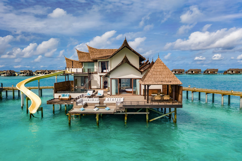 A two-bedroom Ocean Pool RESERVE Sunset with Slide at OZEN RESERVE BOLIFUSHI, its two-storey thatched villa, wide sun deck and curving slide above the turquoise lagoon
