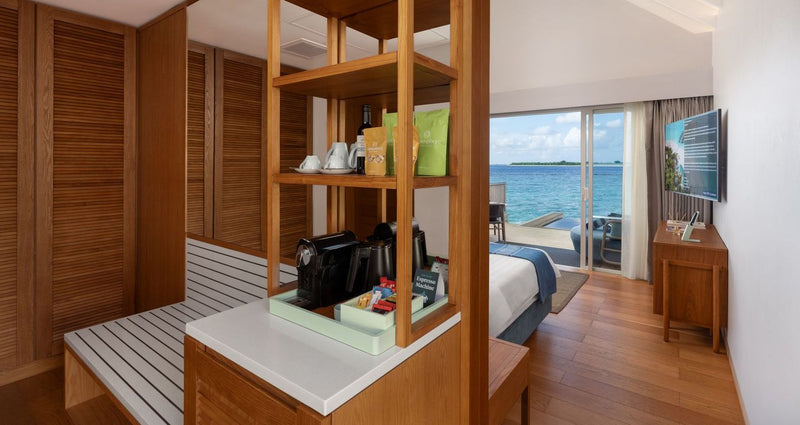 RAAYA by Atmosphere, Raa Atoll: the coffee station and bedroom of a water villa, the sea through the doors