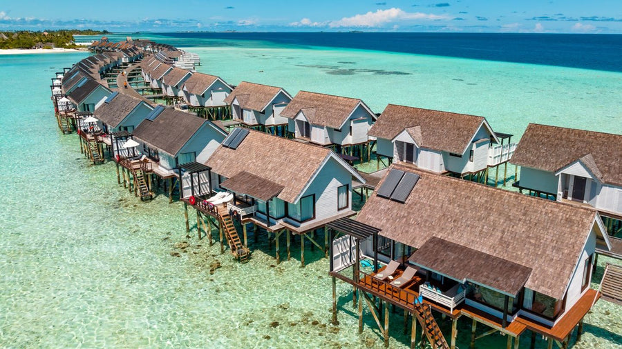 The overwater villas at OZEN LIFE Maadhoo from the air, a long line of thatched villas on stilts above the shallows