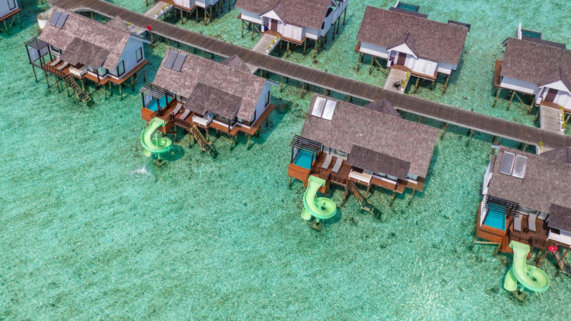 Wind Villas with Jacuzzi & Slide at OZEN LIFE Maadhoo from the air, each with a green slide curling into the lagoon