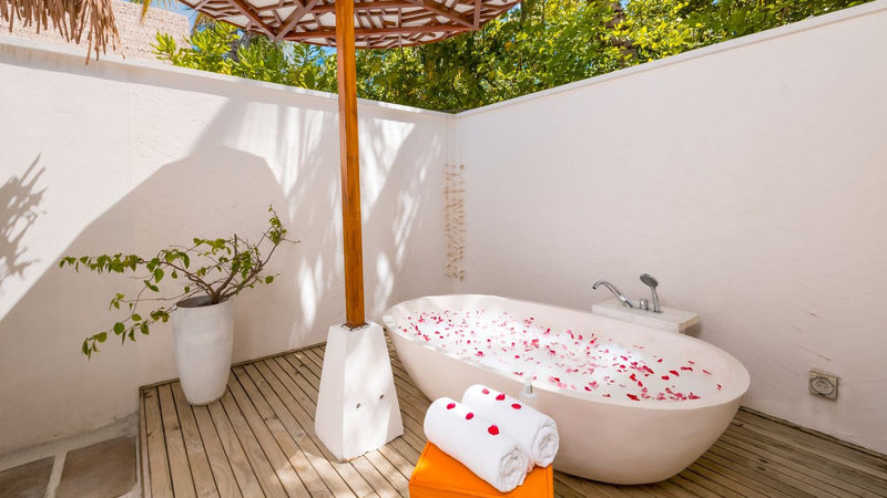 The outdoor bath of an Earth Villa at OZEN LIFE Maadhoo, a freestanding tub scattered with petals on a timber deck inside white garden walls