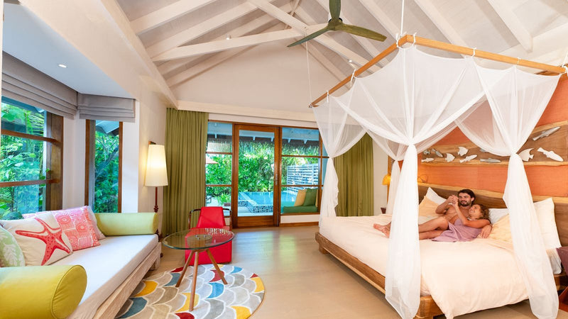 OBLU SELECT Sangeli, North Malé Atoll: a couple in a canopy bed, the villa's garden doors open behind them