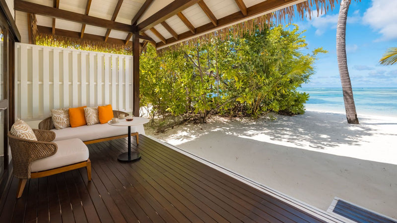 The deck of an Earth Villa at OZEN LIFE Maadhoo, a daybed with orange cushions under the thatch looking out to the beach