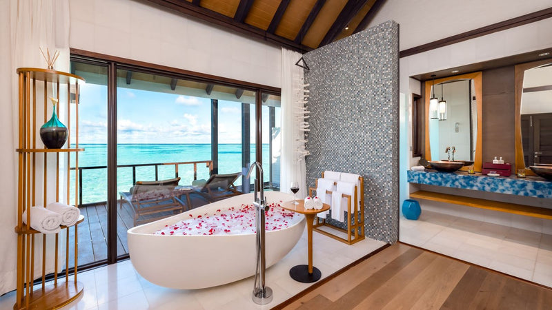 The bathroom of a Wind Villa at OZEN LIFE Maadhoo, a freestanding bath scattered with petals beside doors onto the deck