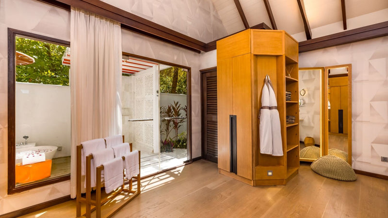 The dressing area of an Earth Villa at OZEN LIFE Maadhoo, robes hanging in a timber wardrobe beside the garden bathroom