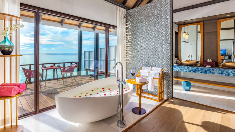 Inside a Wind Villa with Pool at OZEN LIFE Maadhoo, a freestanding bath scattered with petals and folding doors onto the lagoon