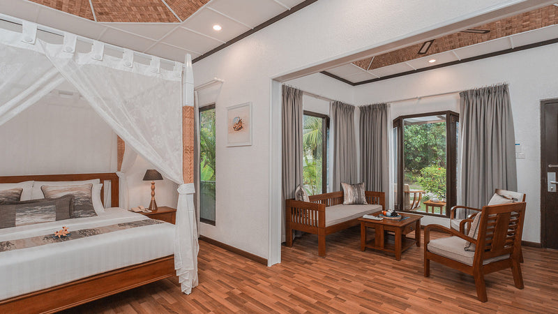 A Deluxe Beachfront Room at Bandos Maldives, with a four-poster bed and a separate sitting area.