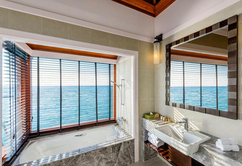 A water villa bathroom at Sheraton Maldives Full Moon, twin basins below shuttered windows over the lagoon.