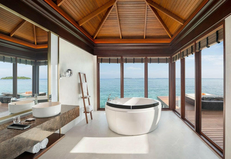 A water villa bathroom at Sheraton Maldives Full Moon, an oval tub set against glass facing the open sea.
