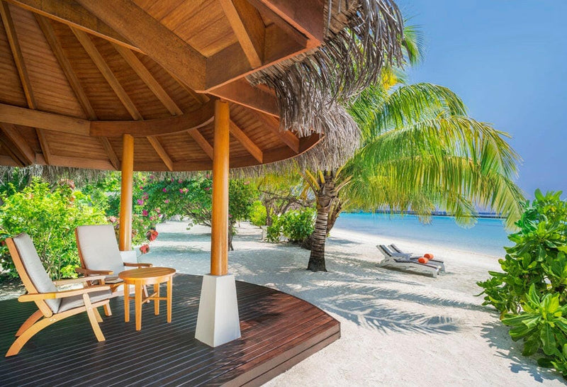 A Beach Front Cottage terrace at Sheraton Maldives Full Moon, recliners under thatch beside leaning palms.