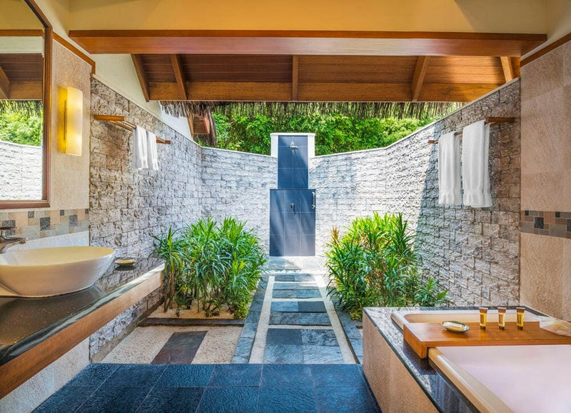 An open air villa bathroom at Sheraton Maldives Full Moon, a stone walled court with a planted water channel.