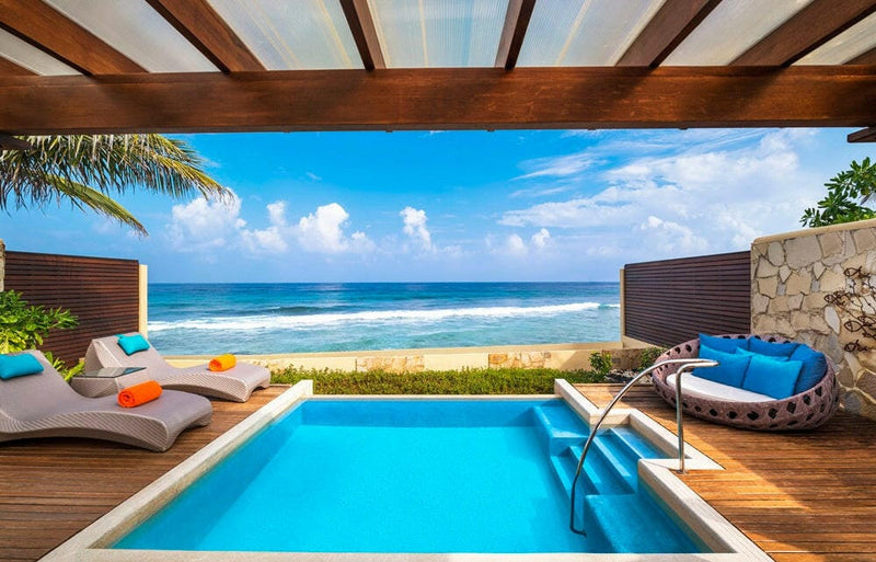 A villa pool at Sheraton Maldives Full Moon, blue cushioned loungers shaded by a timber roof over the sea.