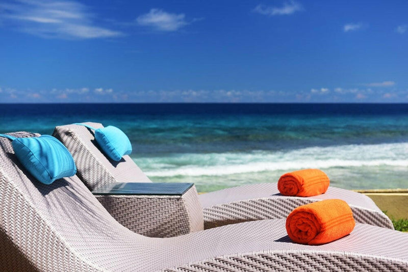 Two loungers at Sheraton Maldives Full Moon, blue cushions and rolled orange towels above the open water.