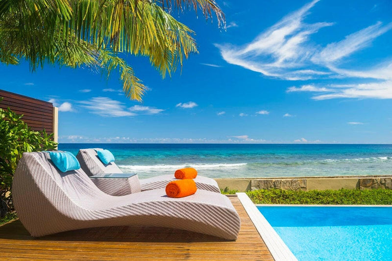 A poolside lounger at Sheraton Maldives Full Moon, orange towels under palm fronds with the sea behind.