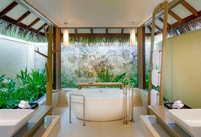 A villa bathroom at Sheraton Maldives Full Moon, an oval tub standing against a wall of green planting.
