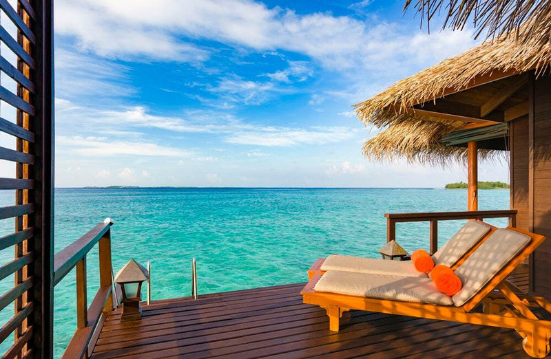 The deck of a water villa at Sheraton Maldives Full Moon, two loungers and orange towels above the lagoon.