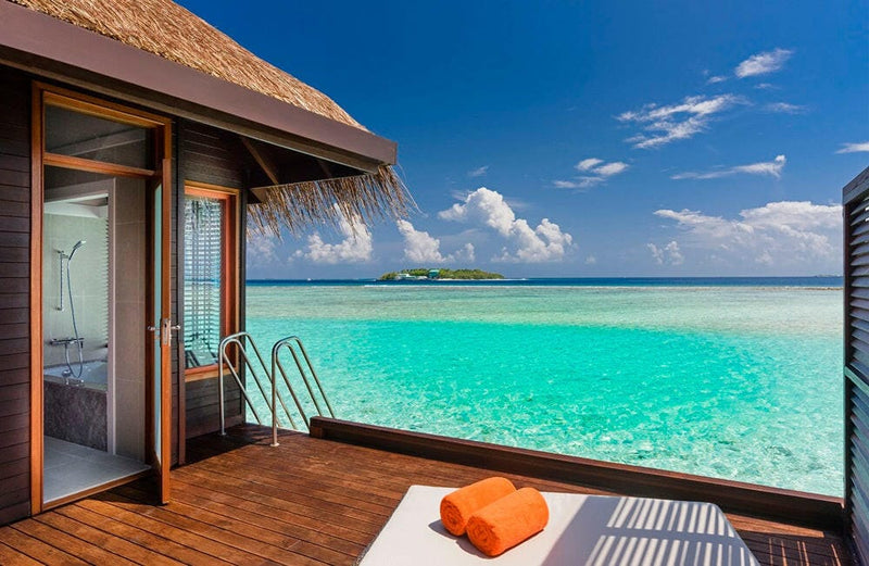 The deck of a water villa at Sheraton Maldives Full Moon, a ladder into turquoise water with an island beyond.
