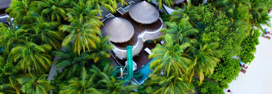 An Oasis Beach Two-bedroom Villa at W Maldives from above, a green tube slide curling down into the villa's pool among palms