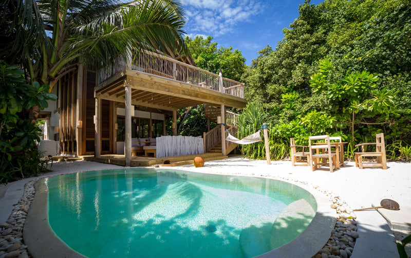 A Two Bedroom Crusoe Suite with Pool at Soneva Fushi, a wooden villa with a curved pool and a dining table under the palms
