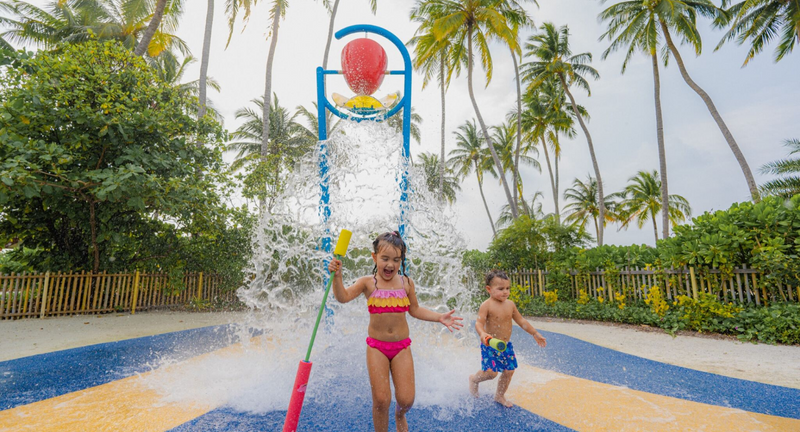 Two children at the water-play bucket in the kids' club splash zone at Avani+ Fares Maldives.
