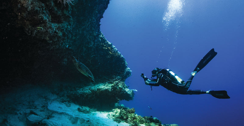 OBLU SELECT Sangeli, North Malé Atoll: a diver swimming past a reef overhang in deep blue water