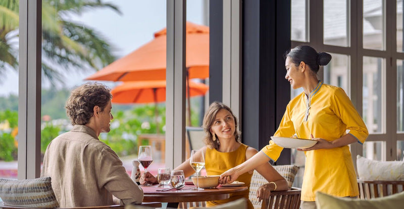 OBLU SELECT Sangeli, North Malé Atoll: a family served lunch on a restaurant terrace under orange umbrellas