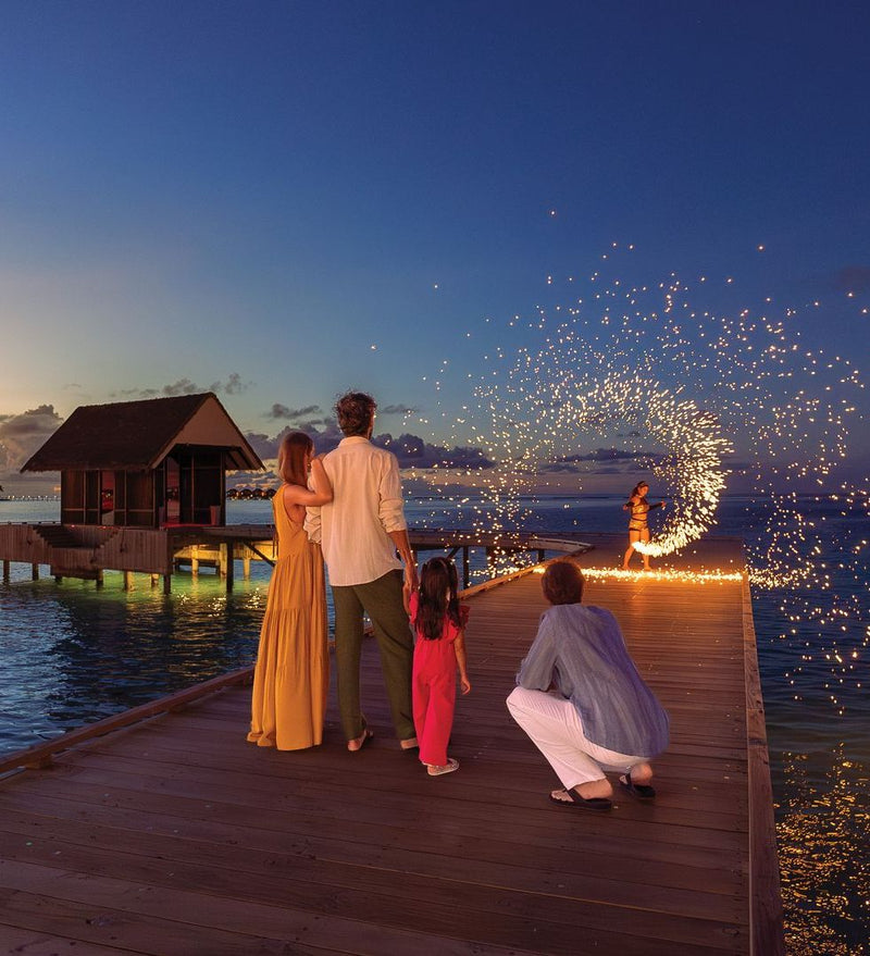 OBLU Xperience Ailafushi, North Malé Atoll: a family watching a fire show on the jetty at dusk