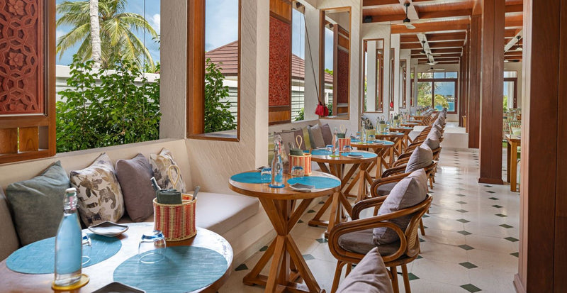 OBLU Xperience Ailafushi, North Malé Atoll: a restaurant with cushioned banquettes and blue-topped tables