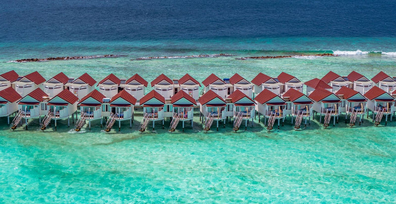 OBLU Xperience Ailafushi, North Malé Atoll: rows of overwater villas with red roofs across the lagoon, seen from the air