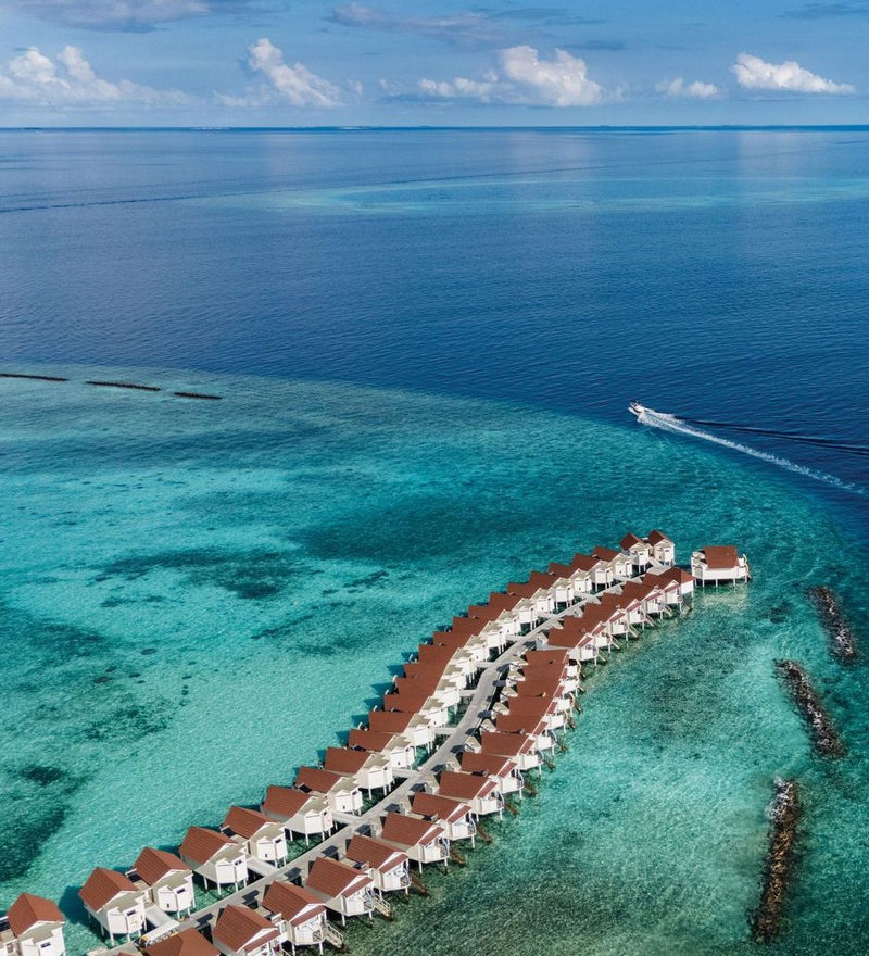 OBLU Xperience Ailafushi, North Malé Atoll: a speedboat crossing the lagoon towards the overwater villas, seen from the air