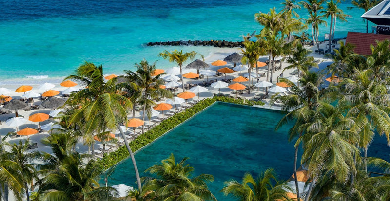 OBLU Xperience Ailafushi, North Malé Atoll: the main pool lined with sunbeds and orange umbrellas, from the air
