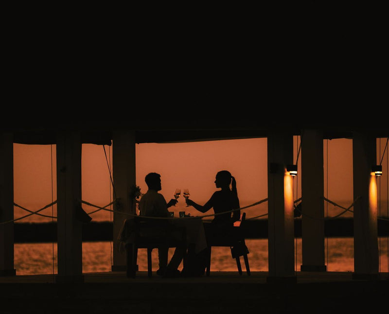 VARU by Atmosphere, North Malé Atoll: a couple toasting at dinner under a deck at sunset