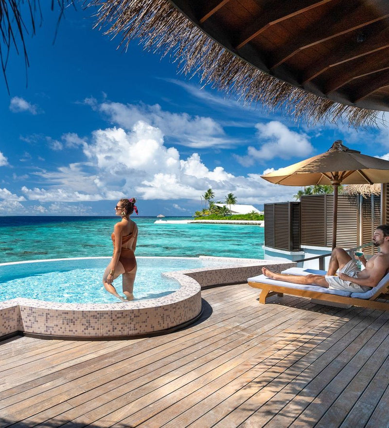 OBLU SELECT Sangeli, North Malé Atoll: a couple at the edge of a villa pool, with the lagoon and a neighbouring island beyond