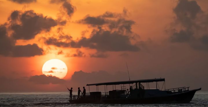 OBLU SELECT Lobigili, North Malé Atoll: a boat silhouetted against the setting sun