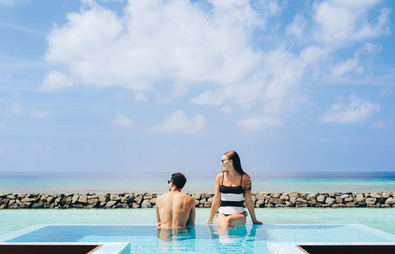 VARU by Atmosphere, North Malé Atoll: a couple at the edge of the main pool, the breakwater and sea beyond