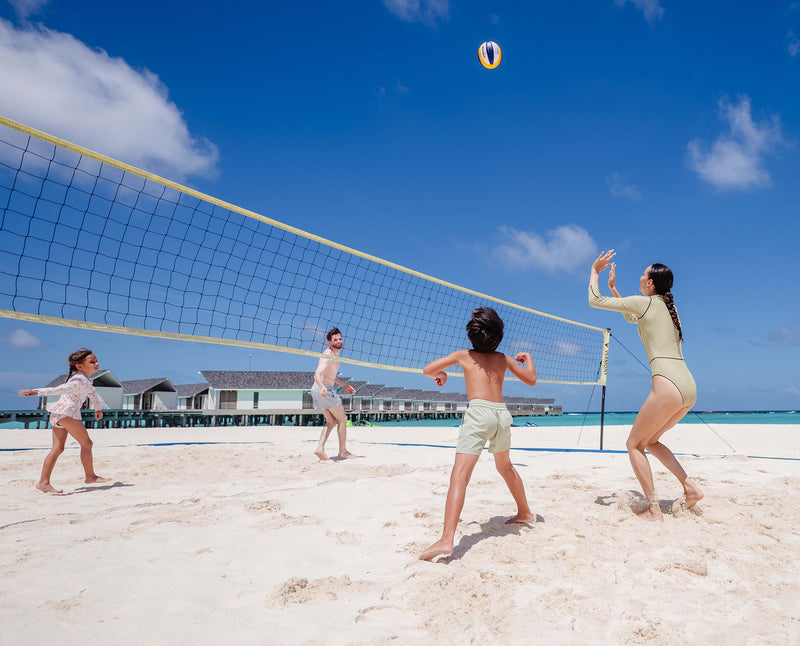 RAAYA by Atmosphere, Raa Atoll: a family playing beach volleyball, the water villas behind