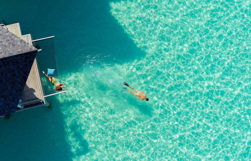 RAAYA by Atmosphere, Raa Atoll: from above, a snorkeller swimming off the steps of a water villa