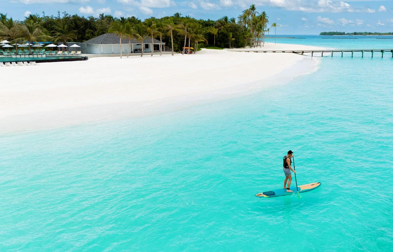 RAAYA by Atmosphere, Raa Atoll: a paddleboarder on the lagoon off the beach