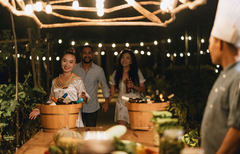 RAAYA by Atmosphere, Raa Atoll: guests with wine at an evening garden event, strung with lights